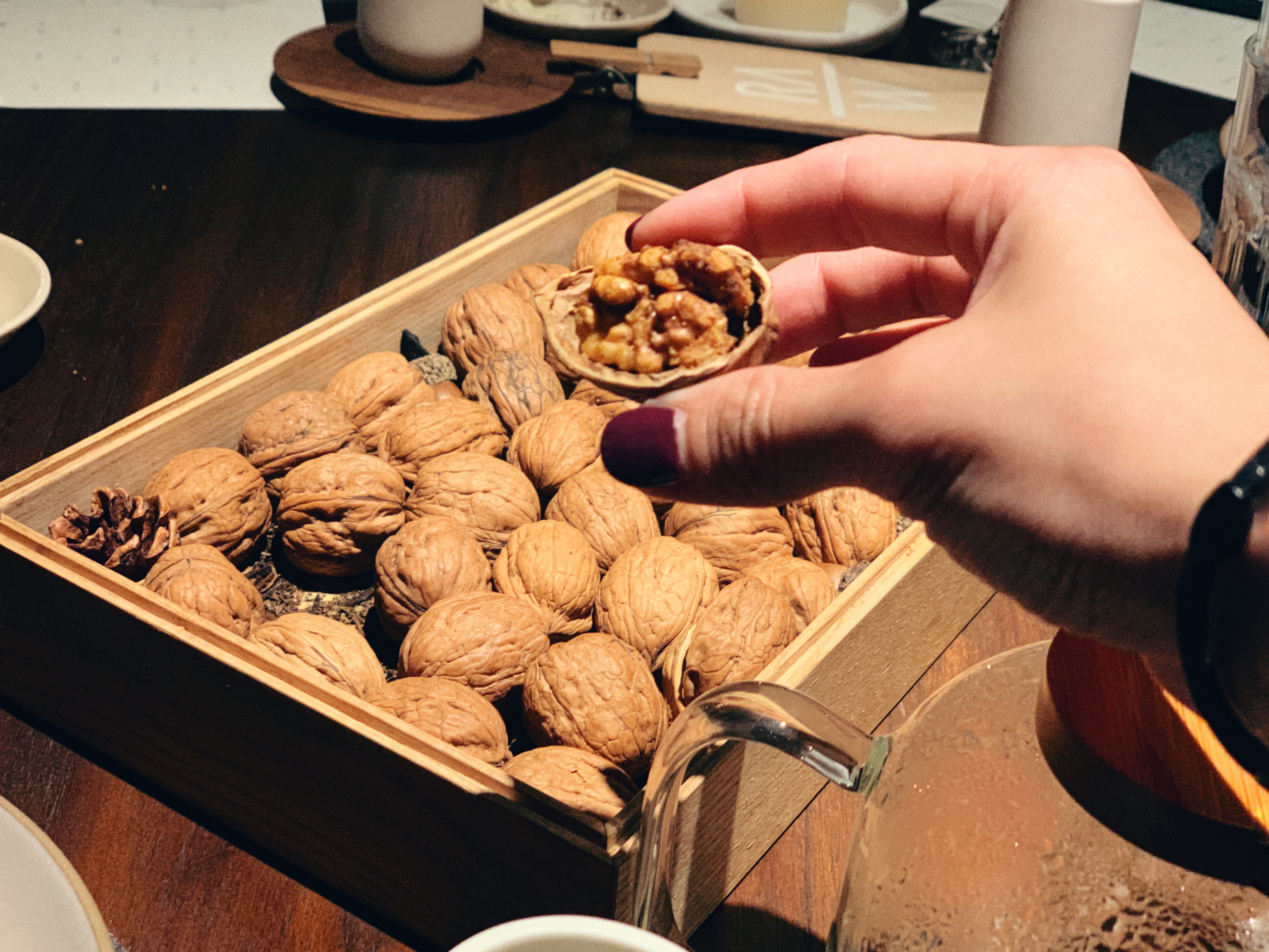 Hand holding a walnut out of a box of walnuts
